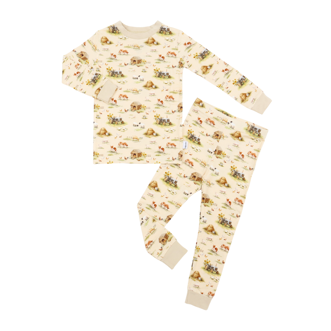 A two-piece children's pajama set featuring a long-sleeve top and matching pants in a warm cream color with a playful all-over print of cartoon animals and landscapes.