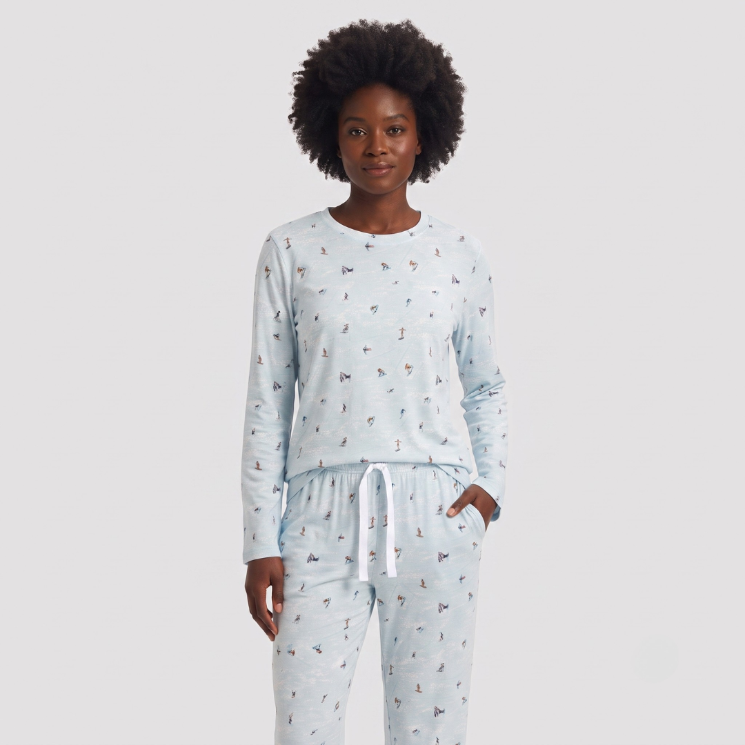 A woman modeling a light blue long-sleeve pajama top and matching pants set with a small all-over print, photographed against a plain light gray studio background.
