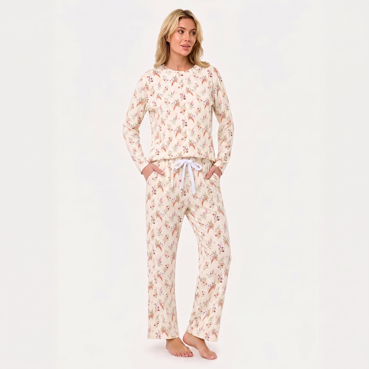 A woman modeling a two-piece long-sleeve pajama set with a cream base and a delicate pink and red floral pattern, featuring a white drawstring waist.