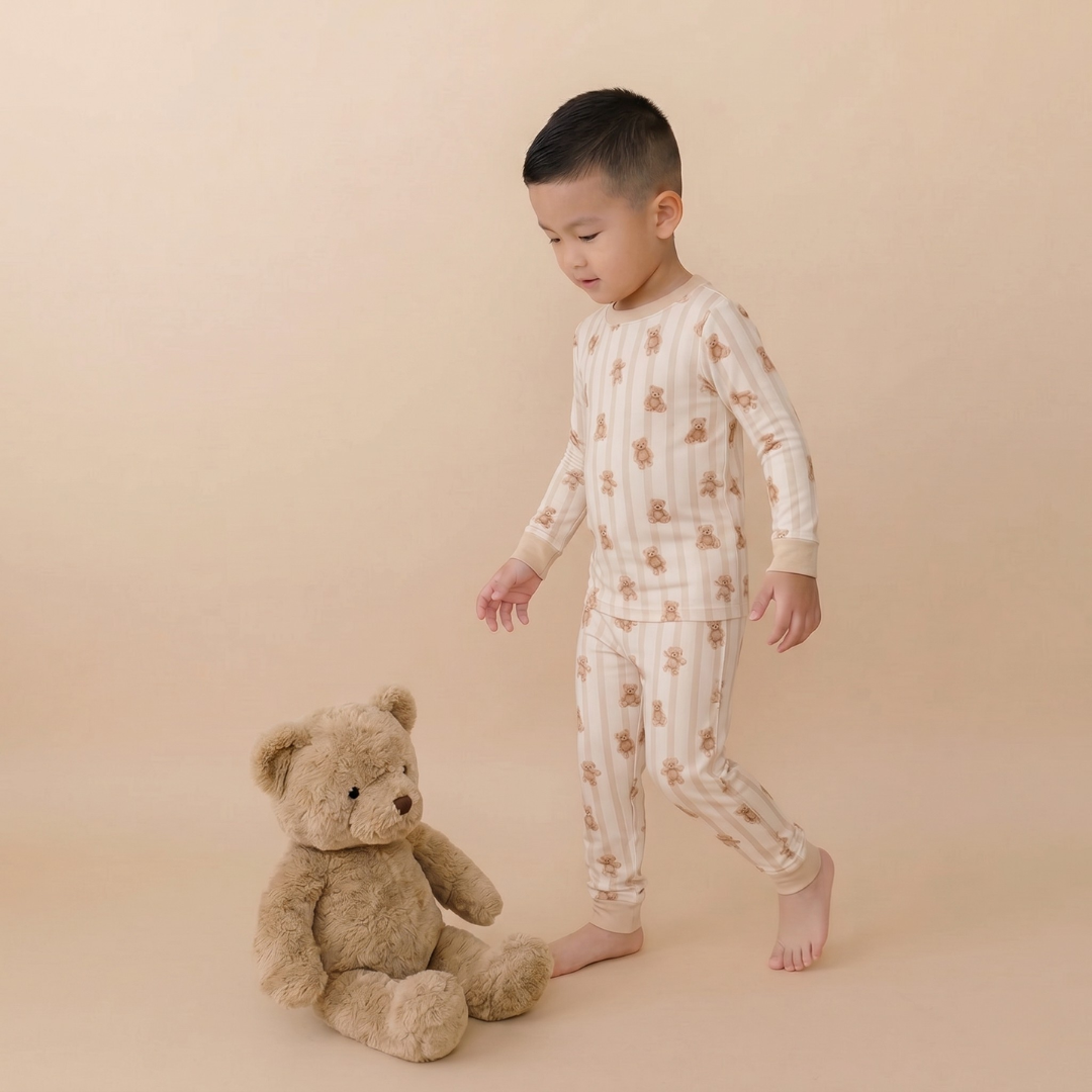 Child in patterned pajamas standing next to a teddy bear on a beige background