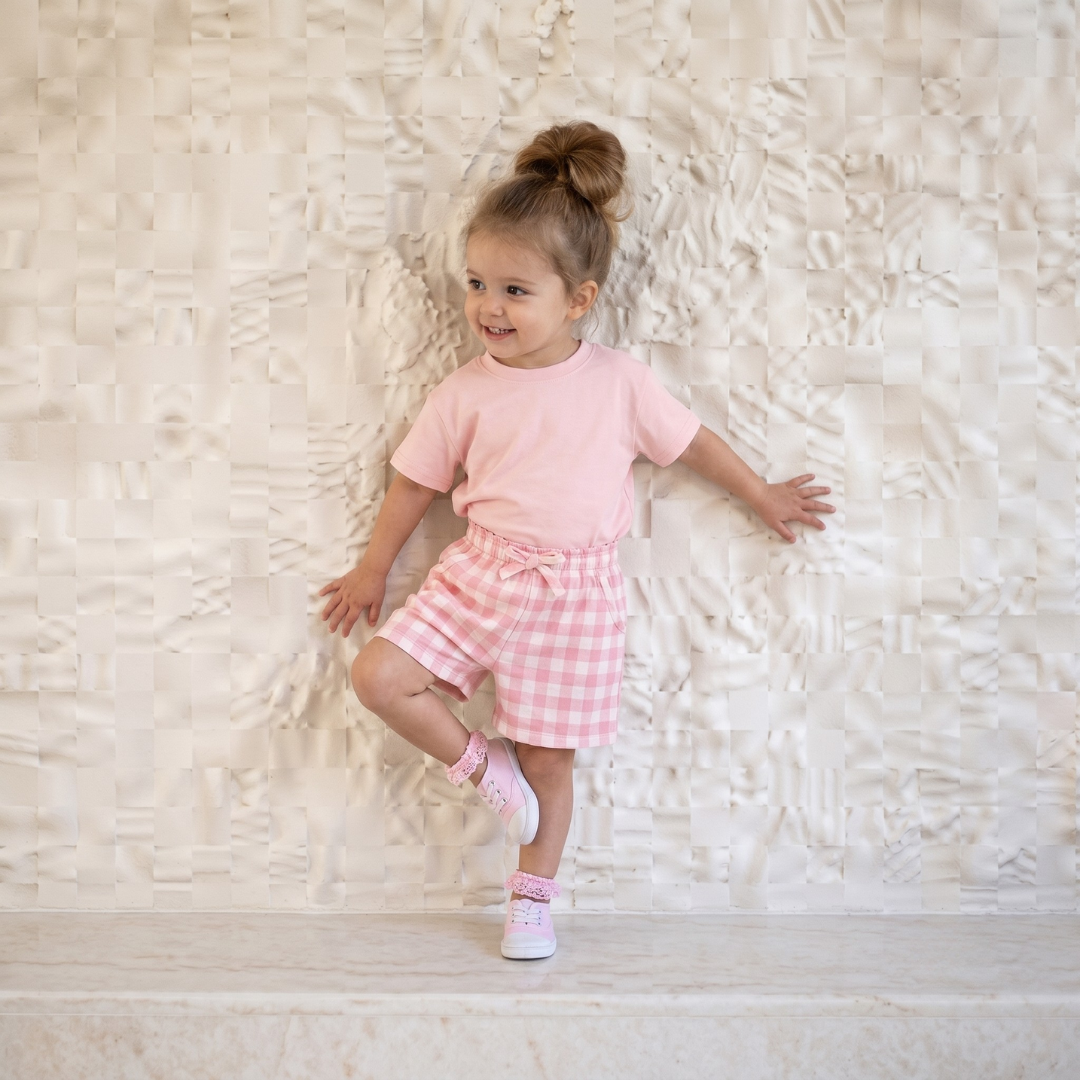 Child wearing a pink outfit with a checkered skirt on a textured white background