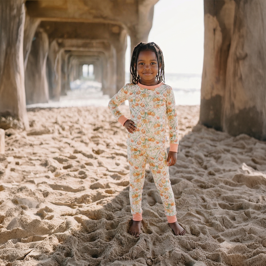 Child in a floral outfit standing on a sandy beach under a pier.